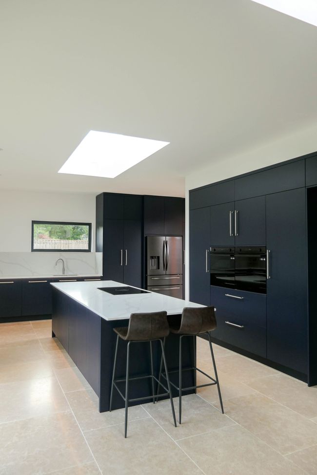 Modern kitchen with dark blue cabinets, a central island with bar stools, stainless steel appliances, marble countertops, and skylights, creating a bright, elegant space.