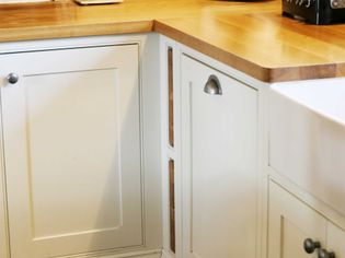 Cream-colored kitchen cabinets with a wooden countertop. The cabinets have simple metal knobs and handles. The tone is warm and inviting.