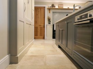 Spacious kitchen with light-coloured cabinetry, a wooden door, and beige tile flooring. The room feels warm and inviting, with modern appliances.