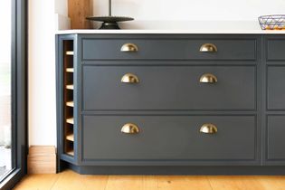 A shaker kitchen sideboard with sleek gray drawers, brass handles, and a built-in wine rack. The countertop is white, giving a crisp, clean look.