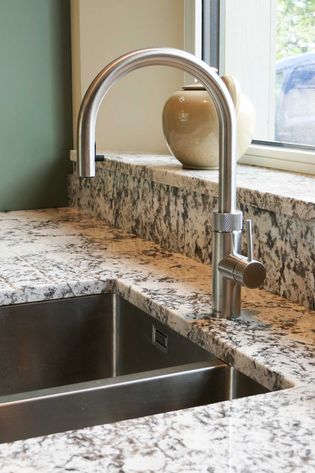 Shaker kitchen sink with a stainless steel tap set in a granite worktop. A beige ceramic vase is placed by the window, creating a serene ambiance.