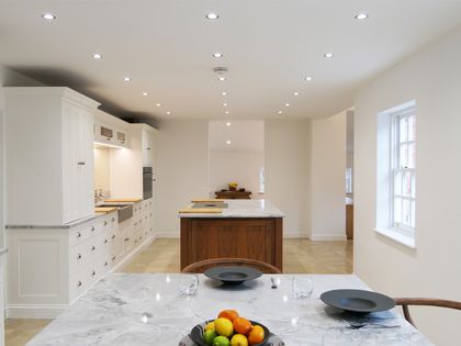 White Shaker kitchen and dining area with a central wood island and a marble table set with dishes and fruit.