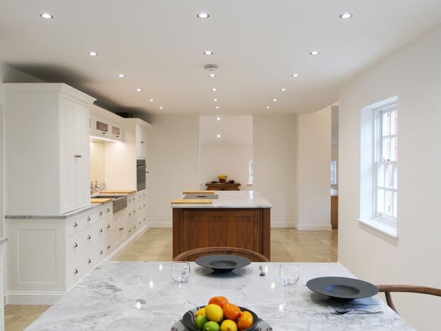 White Shaker kitchen and dining area with a central wood island and a marble table set with dishes and fruit.