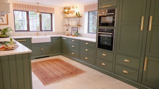 A Shaker kitchen with green cabinetry, a large white farmhouse sink, double ovens, and a decorative rug on the floor.