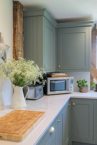 Rustic kitchen corner with a weathered wooden beam beside a soft blue cabinet. White flowers and star decor add a cozy, farmhouse charm.