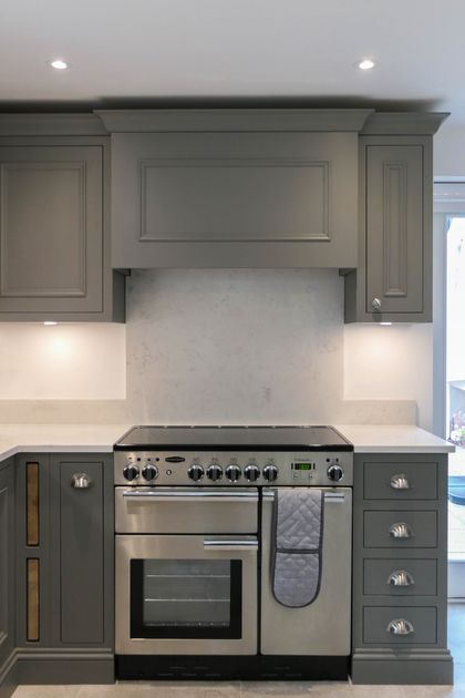 Range cooker fitted into grey Shaker cabinetry with a marble splashback and mantel canopy