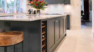 A dark grey shaker island with nickel handles and granite worktop. A wine rack is on the left of the island with a bunch of flowers in a vase on top.