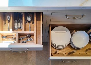 A kitchen drawer with silverware on the left and a drawer with clean white plates on the right.