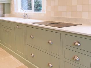 Sleek kitchen with pastel green cabinets, silver cup handles, a modern hob, and a tile backsplash exuding a calm and elegant vibe.