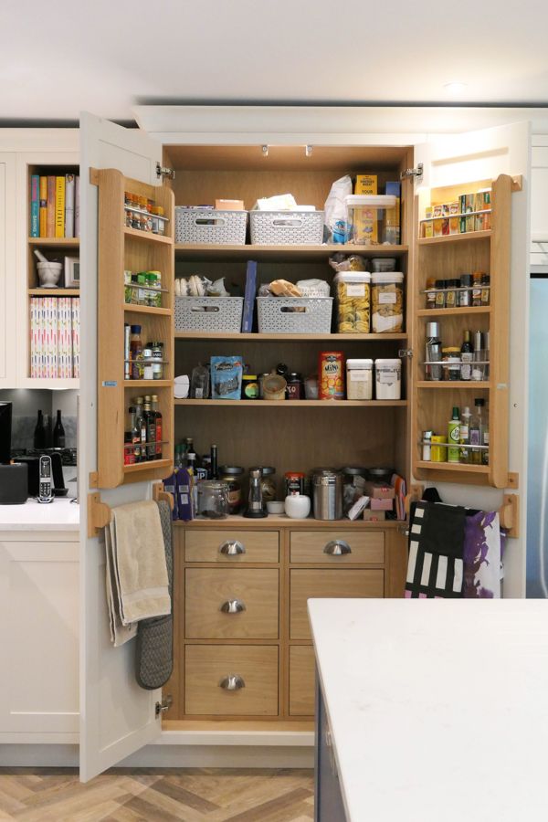 Open pantry with neatly organized shelves, storing canned goods, jars, and baskets. Adjacent stainless steel fridge and colorful cookbook collection nearby.
