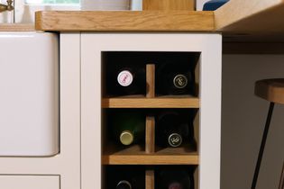 A compact wine rack is integrated into a kitchen cabinet next to the sink. Various wine bottles are stored horizontally. 