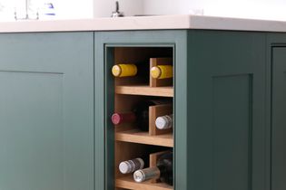 Built-in wine rack with green paneling, holding assorted wine bottles with colorful caps. Modern and elegant kitchen design.