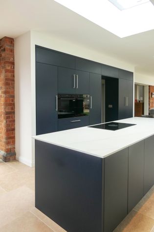Modern kitchen with sleek black cabinets, built-in appliances, and a white marble effect island. Exposed brick accents add warmth to the bright, open space.
