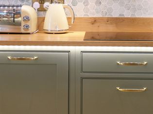 Cream kettle and toaster on a wooden countertop, with hexagonal tile backsplash and green cabinets below..