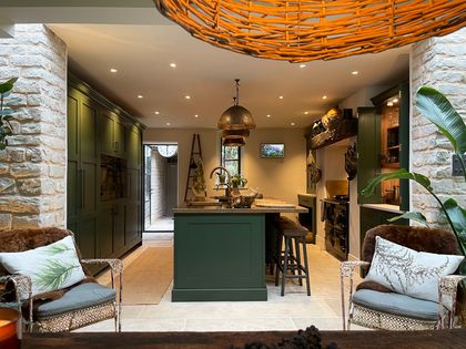 Dark green Shaker kitchen with a copper island, open shelving, stools, and warm pendant lighting.