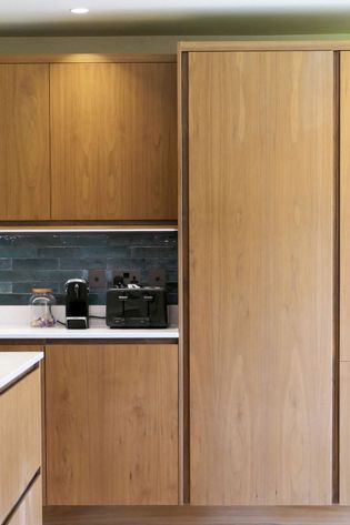 Modern walnut kitchen with a coffee machine and toaster on a white counter beneath dark tile backsplash.