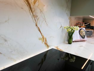 Black induction hob with a marble effect worktop and splash back around, daffodils and a recipe book to the right of the hob