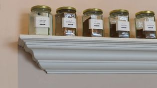 Jars filled with vanilla sugar, cinnamon, nutmeg, cloves, and allspice line a white shelf with ornate molding, conveying an organized, cozy kitchen vibe.