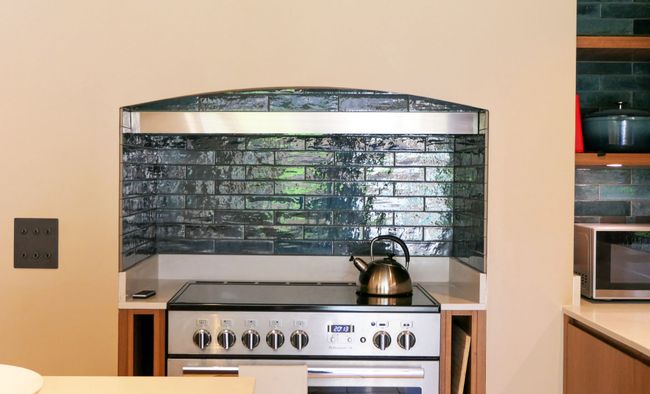 Modern kitchen range with a metallic kettle, dark tiled backsplash, wooden cabinetry, and a microwave.