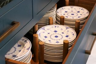 A kitchen drawer filled with neatly stacked blue and white plates on wooden pegs, with additional plates visible behind them.