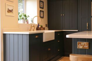 Shaker kitchen with dark grey cabinetry, white farmhouse sink, and brass faucet. Decor includes potted plant, framed art, and wooden accents. 
