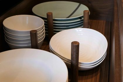 Stacks of plates and bowls held upright by walnut dowels in a peg drawer