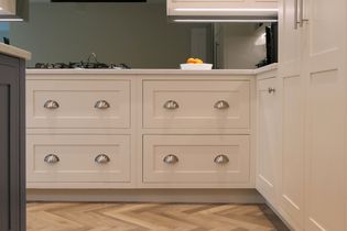 White shaker style cabinetry with silver cup handles, green wall and bowl of fruit on top of the counter.