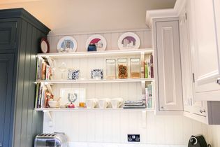 Kitchen shelves with books, glass jars of grains, and decorative plates create a cozy, organized ambiance. Neutral tones highlight elegance.