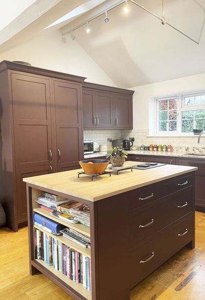 A Shaker kitchen with dark red cabinets, a granite countertop, and a kitchen island displaying a bowl of fruits.