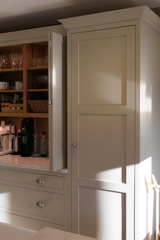 Sunlit kitchen cabinets with an open door reveal shelves of glasses and mugs. A coffee maker sits on the counter, creating a inviting atmosphere.