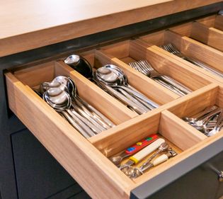 Open wooden drawer organised with spoons, forks, knives, and other utensils.