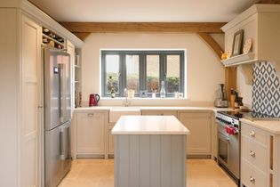 A bright, shaker kitchen with light grey cabinets, a centre island, stainless steel fridge, and stove. A large window allows natural light to fill the space.