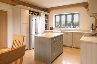 A bright, shaker kitchen with light grey cabinets, a centre island, stainless steel fridge, and stove. A large window allows natural light to fill the space.