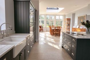 Spacious kitchen and dining area with grey cabinets, white countertops, and skylight. Sunlit dining table, chairs, and garden view add warmth.