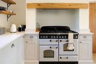 Bright kitchen with a classic black and white range cooker, wooden beam above. White cabinets, shelves with dishes, and appliances.