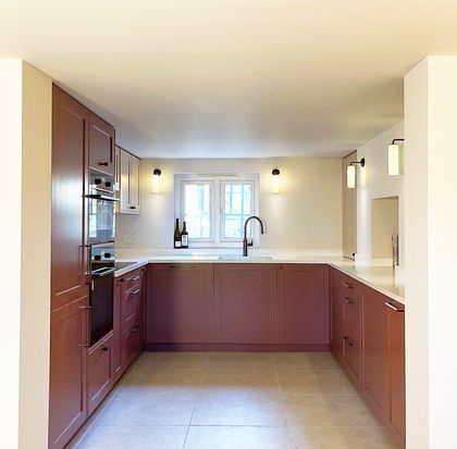 Shaker kitchen with dark red cabinets, white countertops, a central window, and a sink beneath a curved faucet.
