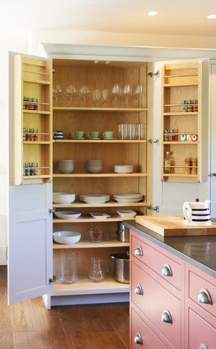 Open larder cupboard stocked with glassware, dishes, cookware, and spice racks on the inside doors.