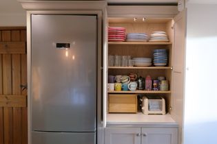 Kitchen with an open cabinet displaying neatly stacked colorful plates, cups, and glasses. A toaster sits on the counter beside the cabinet.