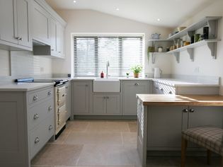 Bright and airy kitchen with grey cabinets, farmhouse sink, and wooden accents. Natural light streams through blinds.
