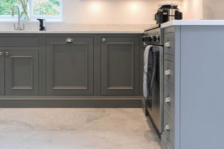 Shaker kitchen with dark grey cabinets and silver handles. An oven with a towel, light countertops, and a window view create a clean, elegant ambiance.