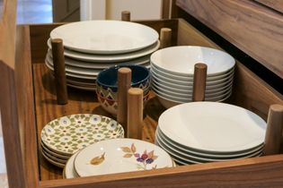 A wooden drawer filled with stacks of white and patterned ceramic plates and bowls between pegs.