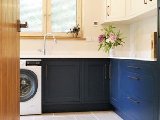 Bright room with navy blue cabinets, a silver sink, washing machine, and a vase of fresh flowers. Light streams through a window with blinds.