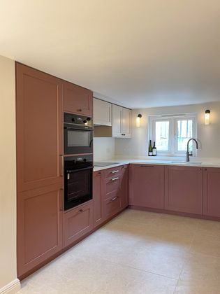 A Shaker kitchen with dark red cabinets, a built-in oven, and a countertop, featuring a sink and two bottles of wine on the counter.