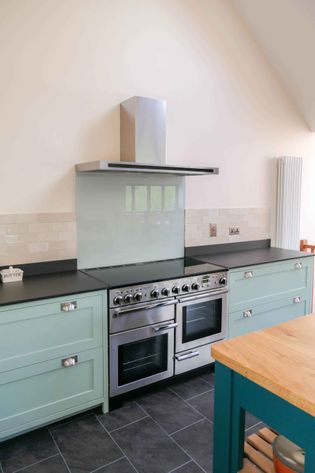 Shaker kitchen with light blue cabinets, a stainless steel oven, and a glass backsplash. Light wooden countertop adds a warm, inviting touch.