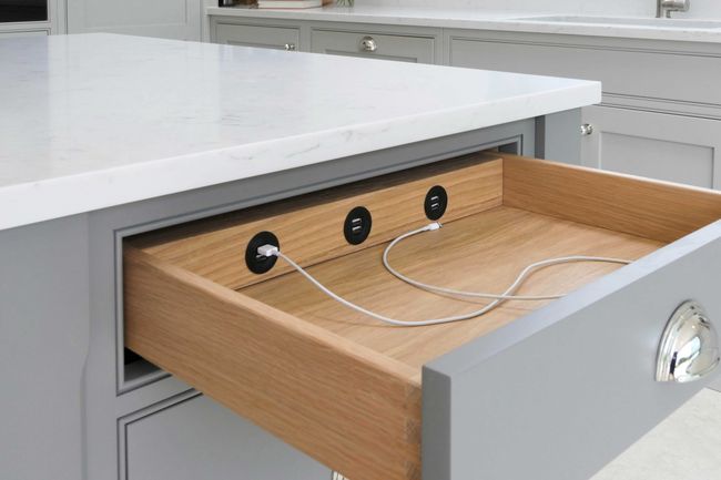 Kitchen island with a light top and open drawer revealing built-in USB ports. Two cables are plugged in, highlighting a sleek, modern design.