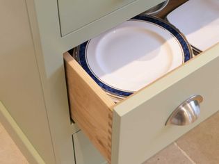 Open sage green drawer showing stack of white plates with a blue rim.