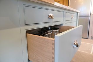 A partially open kitchen drawer reveals neatly stacked stainless steel pots. The cabinetry is pastel green with sleek silver handles, evoking a modern and tidy aesthetic.