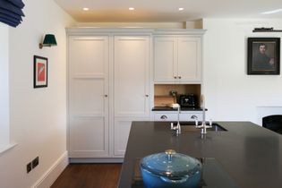 Shaker kitchen with a large island, blue lidded pot, double-faucet sink, cabinetry, framed artwork, and a portrait.