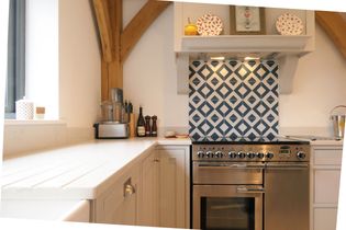 Shaker kitchen with a stainless steel oven, blue geometric tile backsplash, and light grey cabinets. Warm tones and decorative plates.