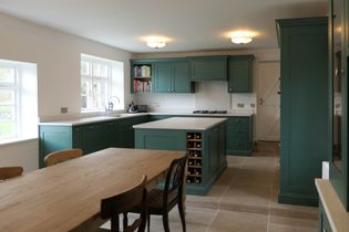 Spacious shaker kitchen with green cabinets, a large wood dining table, and tiled floors. Cozy ambiance with ample natural light and built-in wine rack.